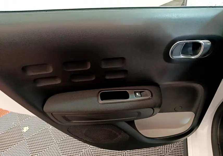Gros plan sur la porte intérieure côté droit de la Citroën C3 blanche, avec poignée chromée et bouton de verrouillage.