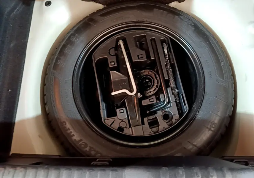 Vue plongeante sur la roue de secours noire et ses outils dans le coffre blanc d'une Citroën C3 2019.
