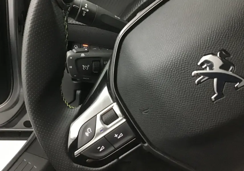 Gros plan sur le volant cuir noir perforé du Peugeot 2008 électrique 2022 avec commandes intégrées et logo lion argenté.