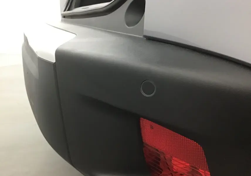 Gros plan sur le feu arrière rouge et le pare-chocs noir du Peugeot 2008 électrique gris Artense, angle arrière droit.