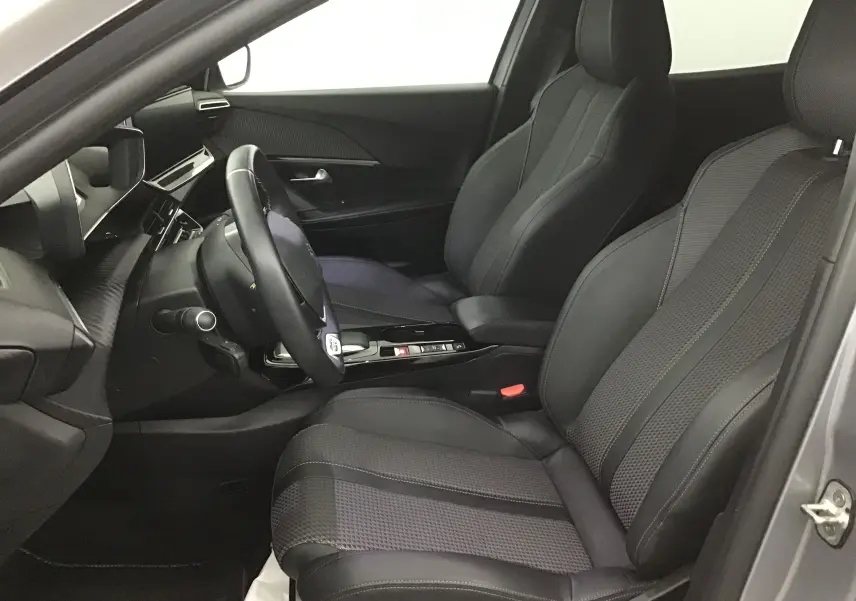Intérieur côté gauche du Peugeot 2008 électrique gris, sièges en cuir noir et tableau de bord moderne avec volant multifonction.