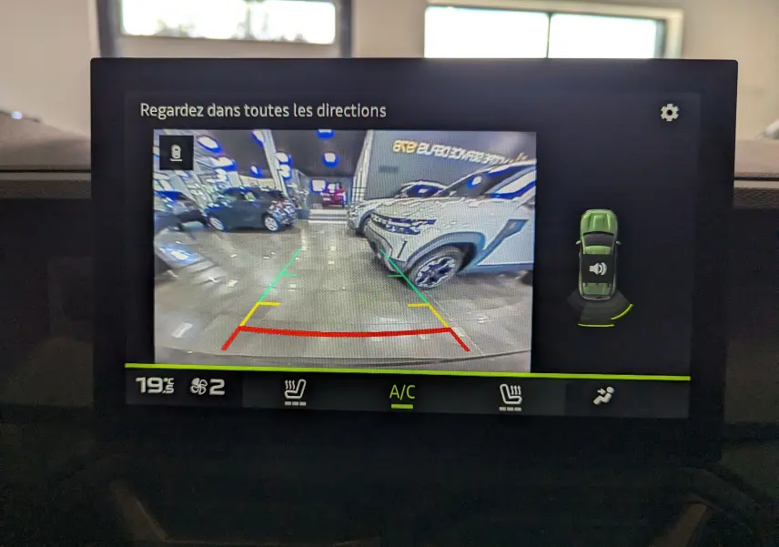 Écran de caméra de recul montrant l'arrière d'un Dacia Duster Gris Schiste dans un showroom lumineux.