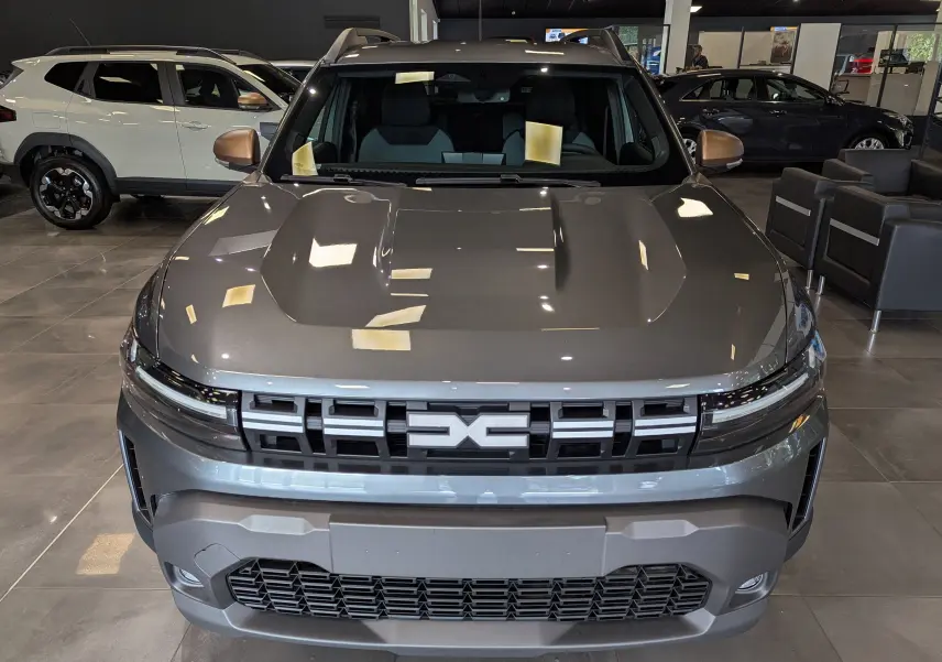 Vue frontale d'un Dacia Duster 2025 gris schiste avec calandre marquée et rétroviseurs bronze en showroom.