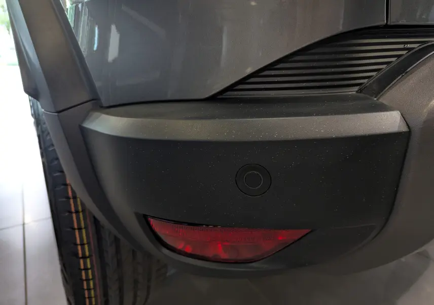 Gros plan sur le pare-chocs arrière gris schiste du Dacia Duster 2025 avec feu antibrouillard et capteur de recul.