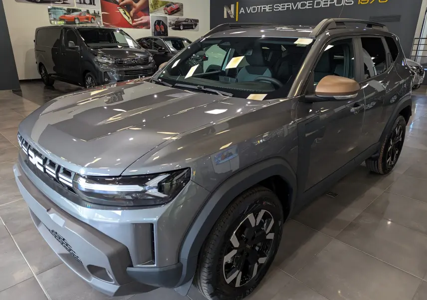 Vue 3/4 avant du Dacia Duster 2025 gris schiste avec rétroviseurs bronze et jantes noires en concession.