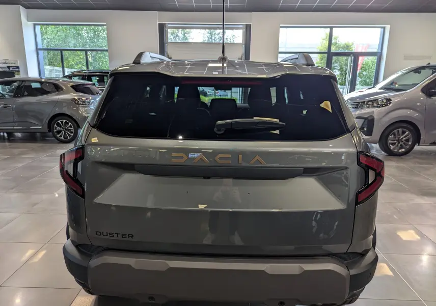 Vue arrière du Dacia Duster 2025 gris schiste en showroom, avec logo doré et feux arrière angulaires distinctifs.