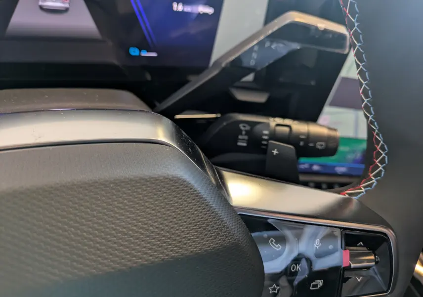 Gros plan sur les commandes au volant du Renault Espace VI hybride, avec coutures tricolores et tableau de bord numérique en arrière-plan.