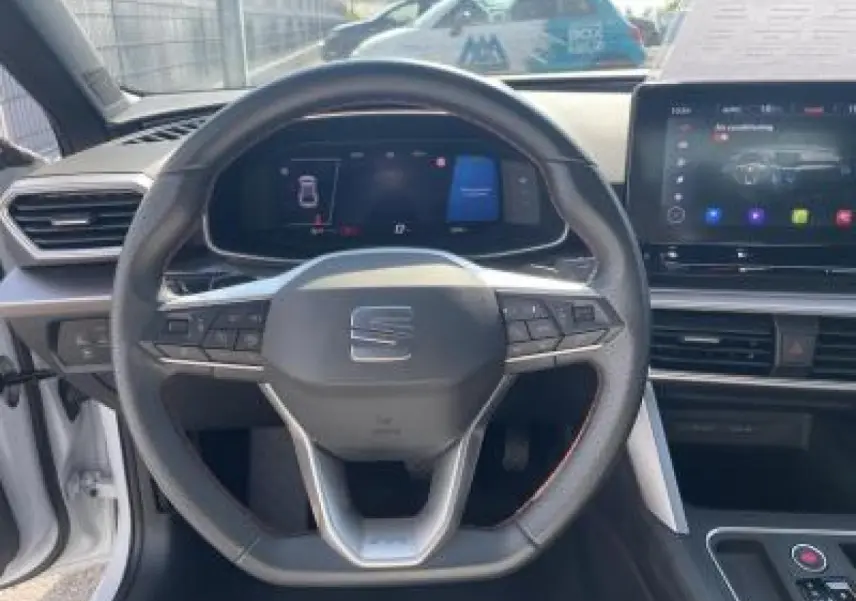 Vue frontale du volant et du tableau de bord digital de la SEAT LEON IV blanche avec écran tactile et commandes au volant.