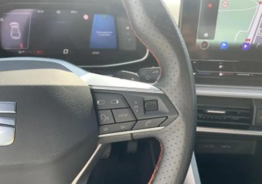 Gros plan sur le volant perforé avec surpiqûres rouges et le tableau de bord digital du SEAT Leon IV blanc Nevada 2024.