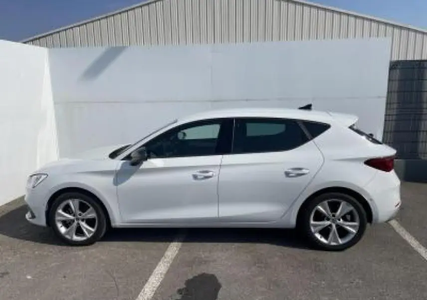 Vue de profil côté gauche d'une SEAT Leon IV blanche Nevada avec jantes alliage 17 pouces, garée en extérieur.