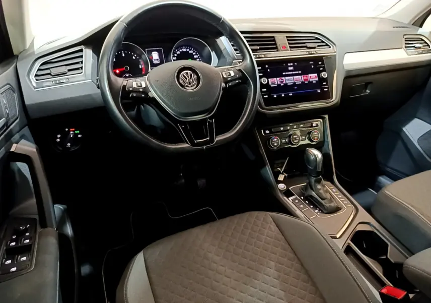 Vue intérieure du tableau de bord et volant cuir noir du Volkswagen Tiguan gris clair avec écran tactile central.