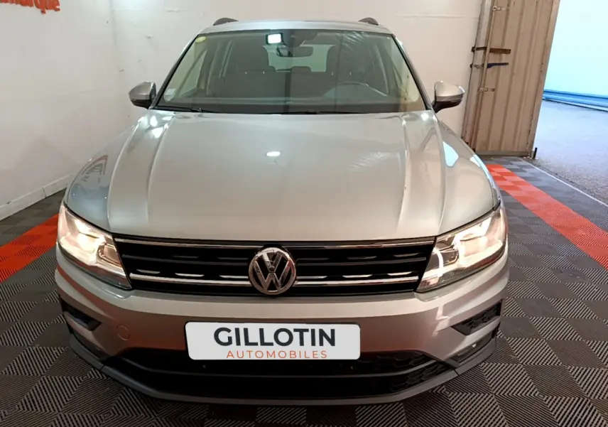 Vue frontale d'un Volkswagen Tiguan gris clair 2020 avec phares allumés et calandre noire brillante.