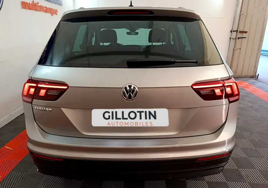 Vue arrière d'un Volkswagen Tiguan gris clair avec feux LED allumés et logo VW visible sur un sol à damiers.