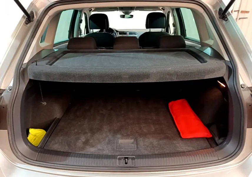 Coffre ouvert vu de l'arrière d'un Volkswagen Tiguan gris clair avec cache-bagages et objets rouges et jaunes.