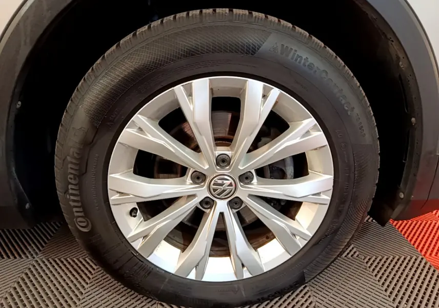 Gros plan sur la roue avant droite d'un Volkswagen Tiguan gris clair avec jante alliage et pneu Continental hiver.