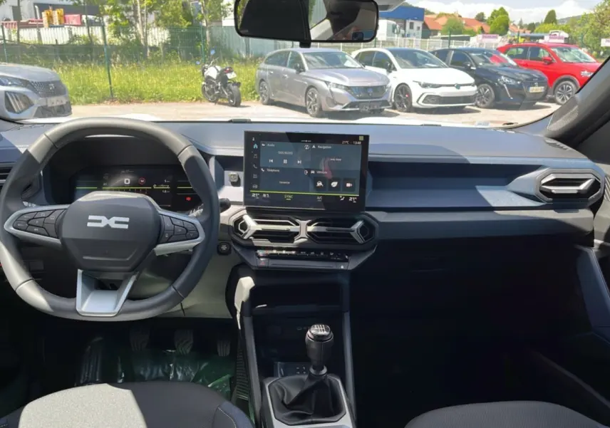 Intérieur du Dacia Bigster blanc glacier 2025, vue du poste de conduite avec volant multifonction et écran tactile central.