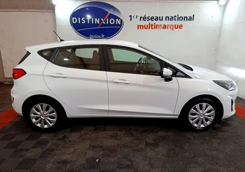 Vue de profil côté gauche d'une Ford Fiesta blanche 2022 dans un showroom avec logo Distinxion en arrière-plan.