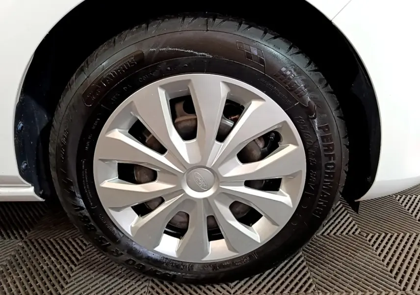 Gros plan sur la roue avant gauche d'une Ford Fiesta blanche, mettant en valeur la jante et le pneu noir.