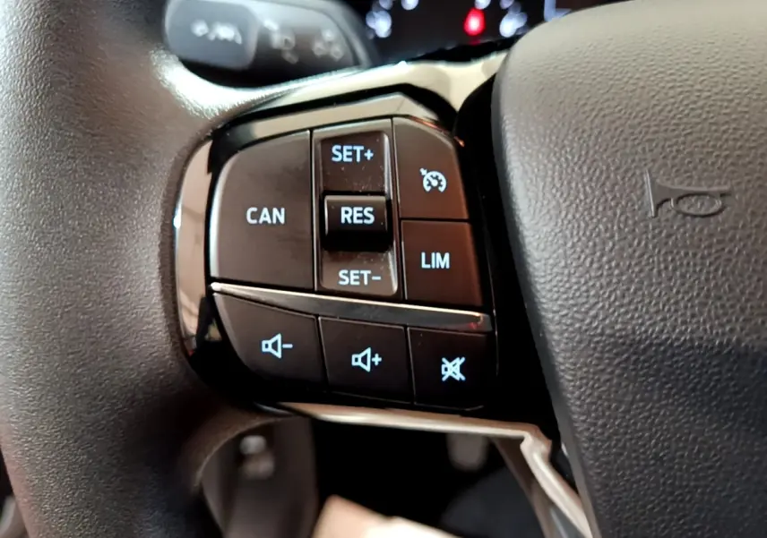 Gros plan sur les commandes du régulateur de vitesse et du volume audio sur le volant noir d'une Ford Fiesta blanche.