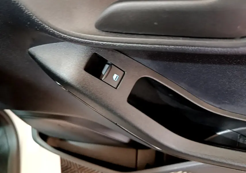 Gros plan sur le bouton de commande de lève-vitre côté conducteur dans l’habitacle noir de la Ford Fiesta blanche.