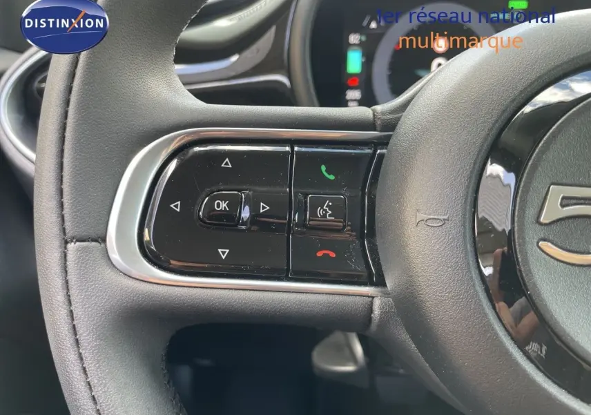 Gros plan sur les commandes gauche du volant noir de la Fiat 500 électrique 2023, avec boutons multifonctions et finition brillante.