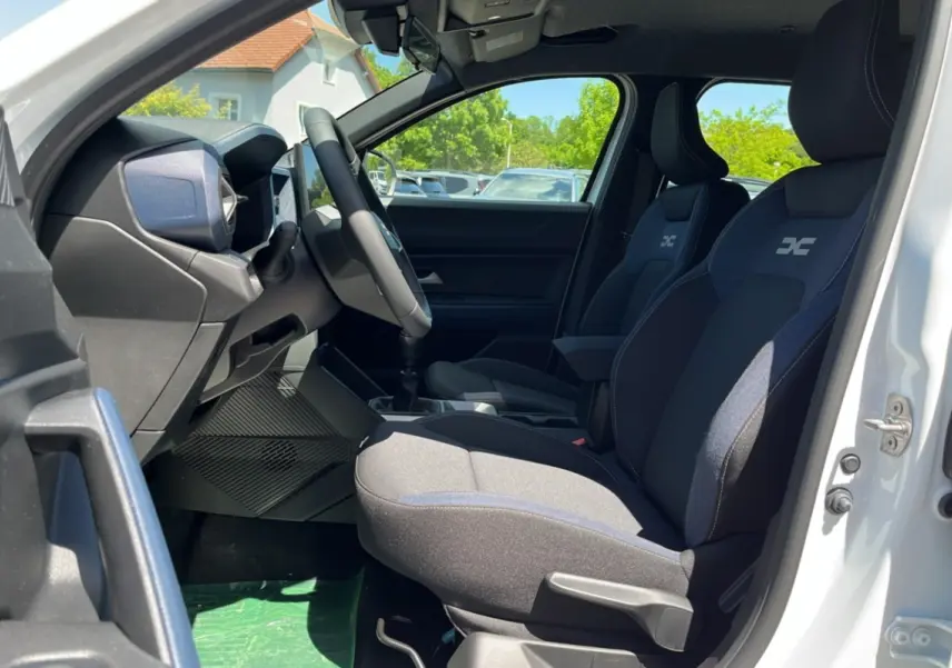 Intérieur avant droit du Dacia Bigster blanc glacier 2025, sièges tissu avec logo, volant cuir et tableau de bord moderne.