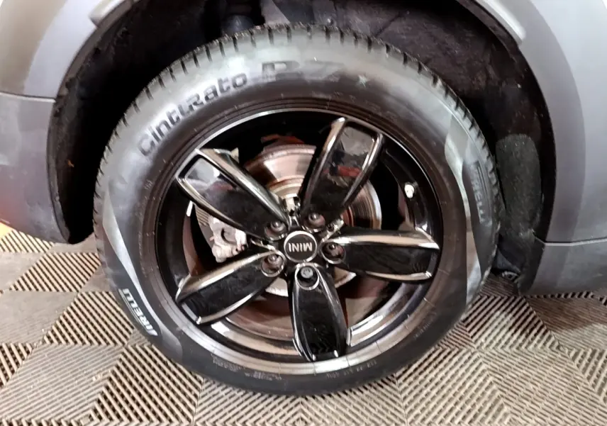 Gros plan sur la roue avant droite du MINI Countryman gris clair, jante noire brillante à cinq branches.