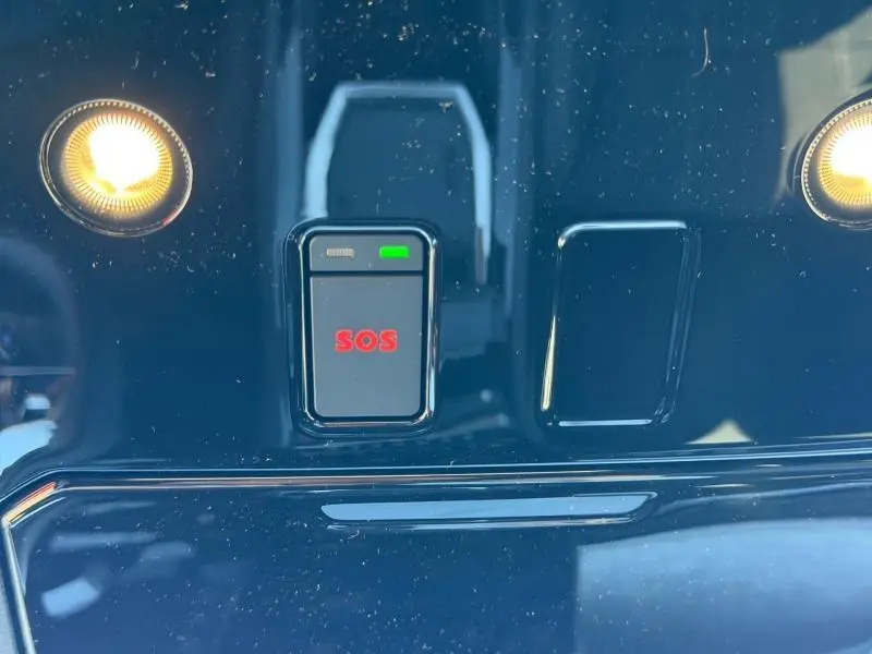 Gros plan sur le bouton SOS rouge encadré de noir, avec éclairage ambiant sur fond brillant noir du tableau de bord.