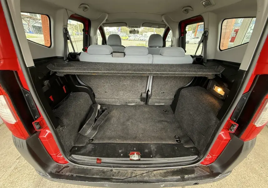 Coffre ouvert vu de l'arrière d'un Peugeot Bipper Tepee rouge avec banquette grise et tapis de coffre noir.