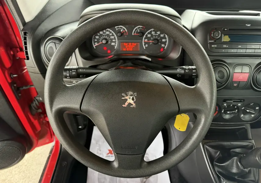 Vue intérieure centrée sur le volant Peugeot d'un Bipper Tepee rouge, avec tableau de bord et console radio visibles.