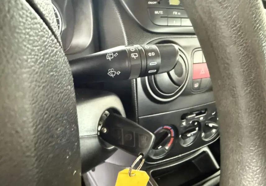 Gros plan sur le volant et la clé de contact d'un Peugeot Bipper Tepee rouge, avec commandes de climatisation visibles.