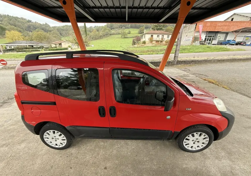 Profil droit du Peugeot Bipper Tepee rouge, avec portes coulissantes et jantes 15 pouces sous abri.