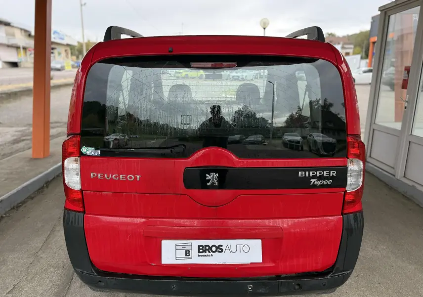 Vue arrière du Peugeot Bipper Tepee rouge avec logo et plaques visibles sous un abri urbain.