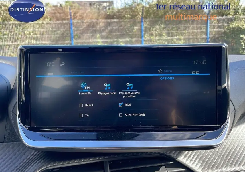 Écran tactile central du tableau de bord du Peugeot 2008 blanc, affichant les réglages audio FM en extérieur lumineux.