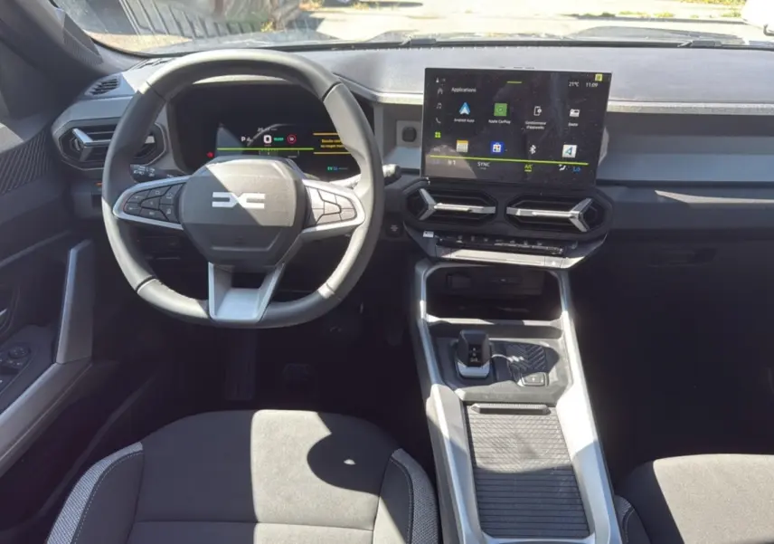 Intérieur du DACIA BIGSTER Hybrid 155 Journey City, vue frontale du poste de conduite avec écran tactile et volant cuir.
