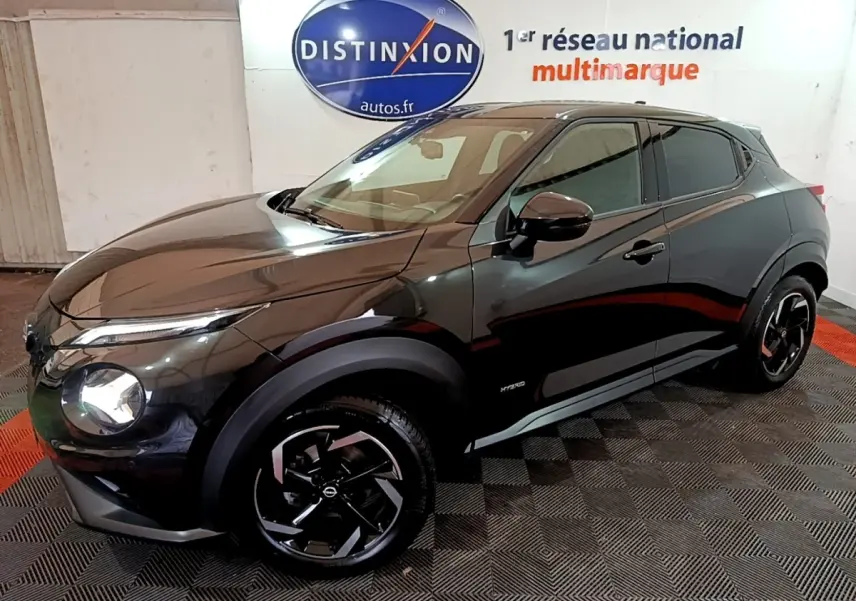Nissan Juke Hybrid 143 Business+ noir vu de 3/4 avant droit, avec jantes noires et logo Distinxion en arrière-plan.