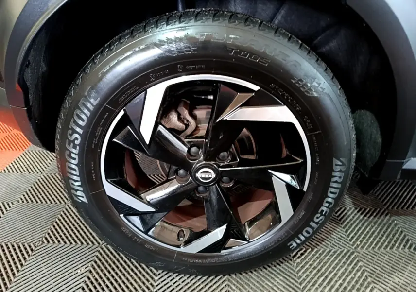 Gros plan sur la roue avant droite du Nissan Juke Hybrid 143 Business+ noire, jante alliage noire et argentée, pneu Bridgestone.