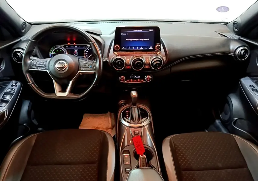Vue intérieure frontale du tableau de bord et volant cuir noir du Nissan Juke Hybrid 2022 avec écran tactile central allumé.