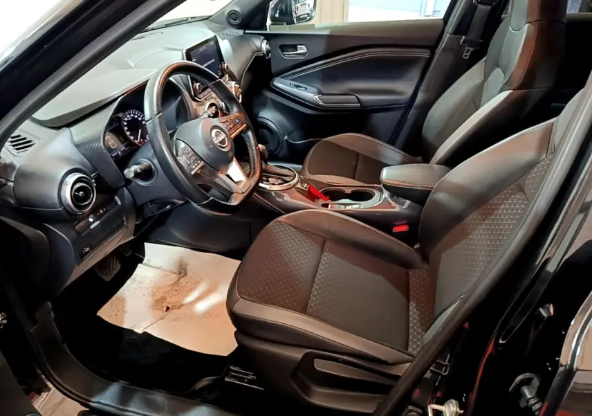 Vue intérieure côté conducteur du Nissan Juke Hybrid 143 Business+ noir, avec tableau de bord et sièges avant en tissu noir.
