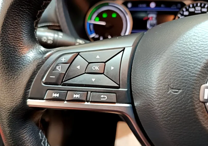 Gros plan sur les commandes gauche du volant cuir noir du Nissan Juke Hybrid 143 Business+ 2022 avec tableau de bord en arrière-plan.