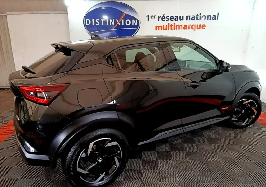 Vue 3/4 arrière droite d'un Nissan Juke Hybrid 143 Business+ noir brillant avec jantes noires et logo Hybrid visible.