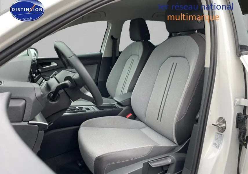 Vue intérieure côté conducteur de la SEAT LEON IV blanche 2024, sièges tissu gris clair avec détails noirs.