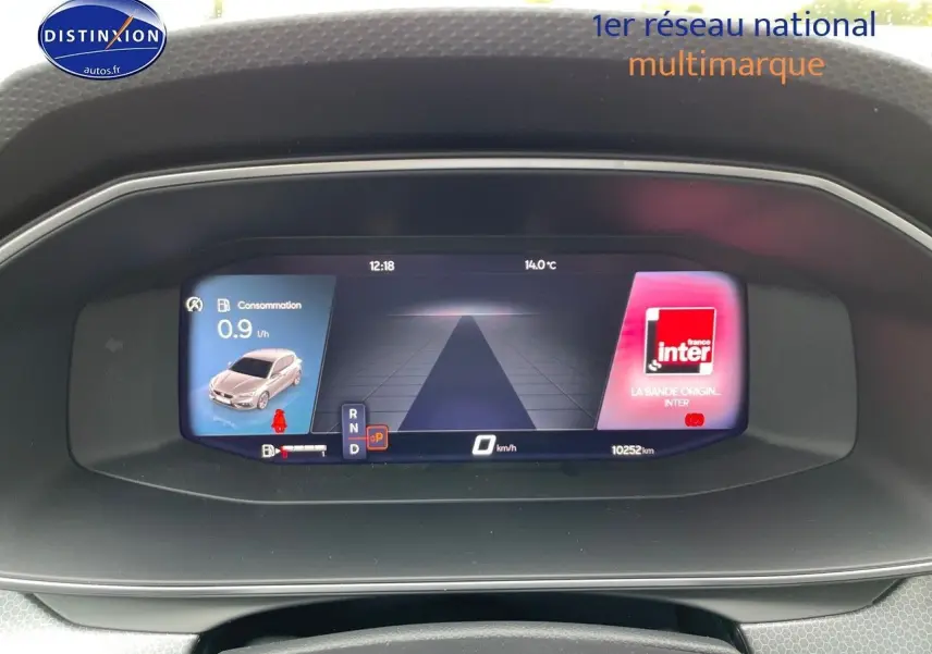 Tableau de bord numérique de la SEAT LEON IV blanc, affichant consommation, vitesse et radio en vue frontale.