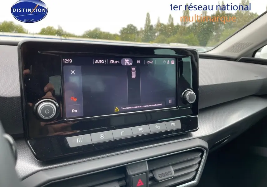 Vue intérieure du tableau de bord de la SEAT LEON IV blanche, avec écran tactile central et commandes climatisation visibles.