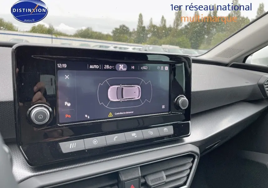 Tableau de bord de la SEAT LEON IV blanche 2024, avec écran tactile affichant l'aide au stationnement et commandes intégrées.