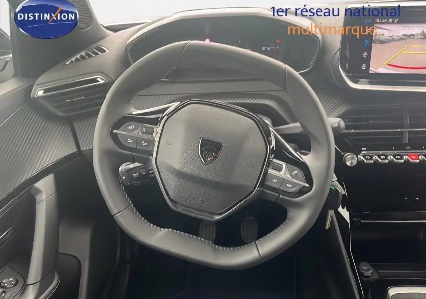 Vue rapprochée du volant cuir noir du Peugeot 2008 blanc Okenite, avec tableau de bord et écran multimédia affichant la caméra de recul.