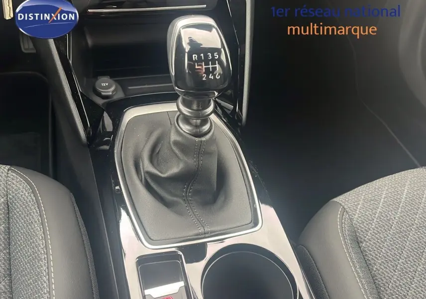 Le levier de vitesses manuel noir au centre de la console d'une Peugeot 2008 blanche, avec sièges gris en tissu.