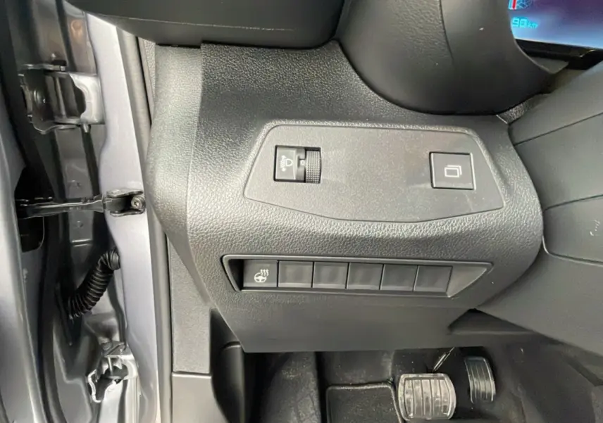 Gros plan sur les commandes côté gauche du tableau de bord du Citroën Berlingo 2025 gris artense, avec pédales visibles.