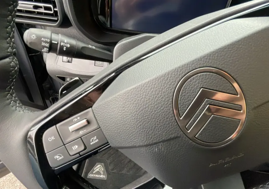 Gros plan sur le volant en cuir du Citroën Berlingo 2025, avec commandes intégrées et logo chromé central.