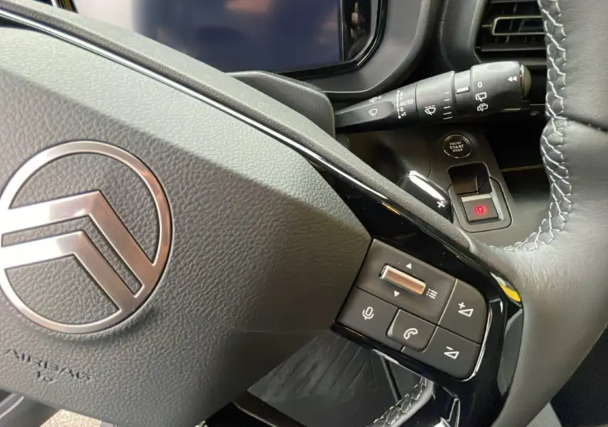 Gros plan sur le volant en cuir du Citroën Berlingo 2025 gris artense avec commandes audio et bouton start/stop visibles.